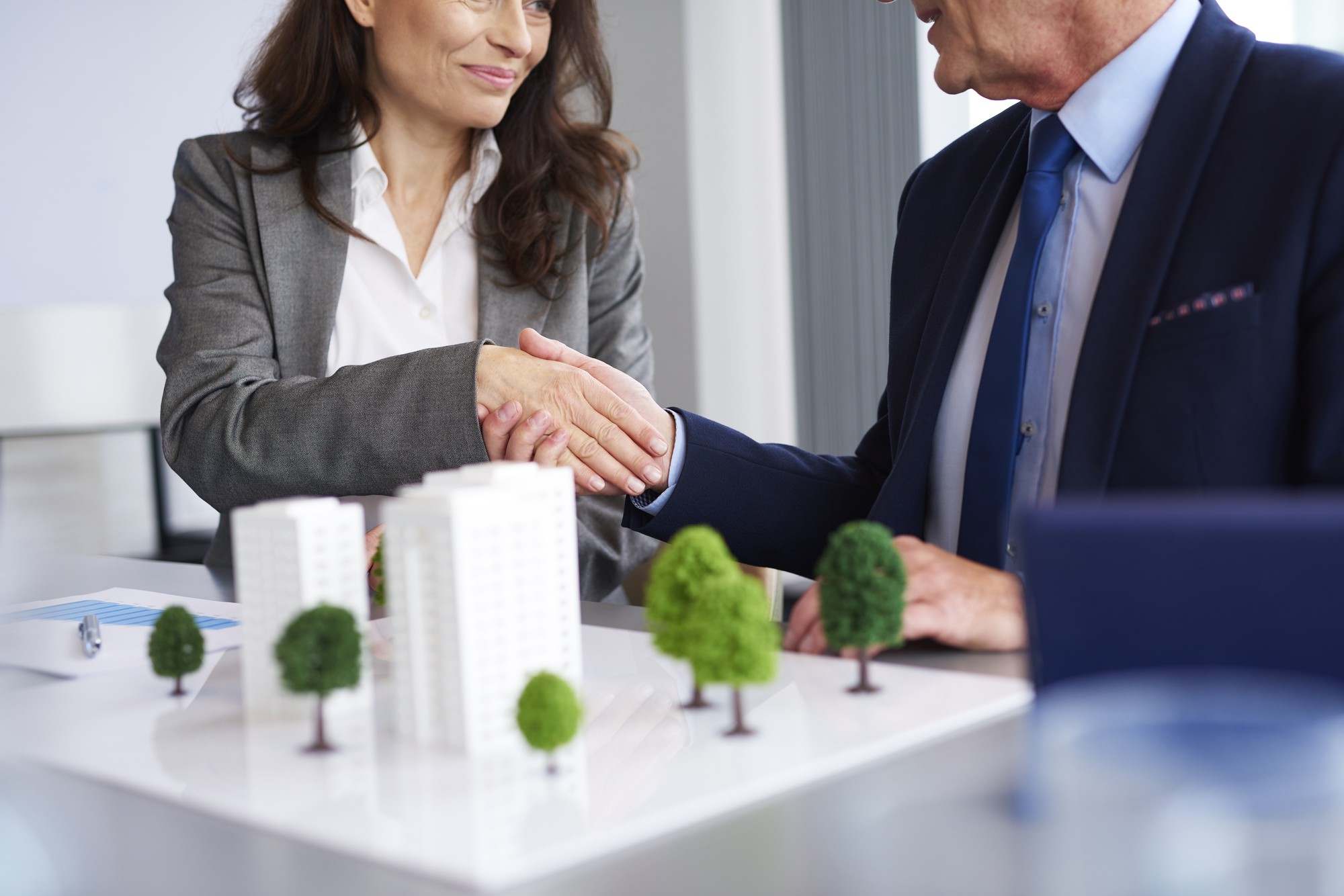 Two business professionals shaking hands over a real estate model, symbolizing successful deals with a Top Real Estate Agent in Orange County