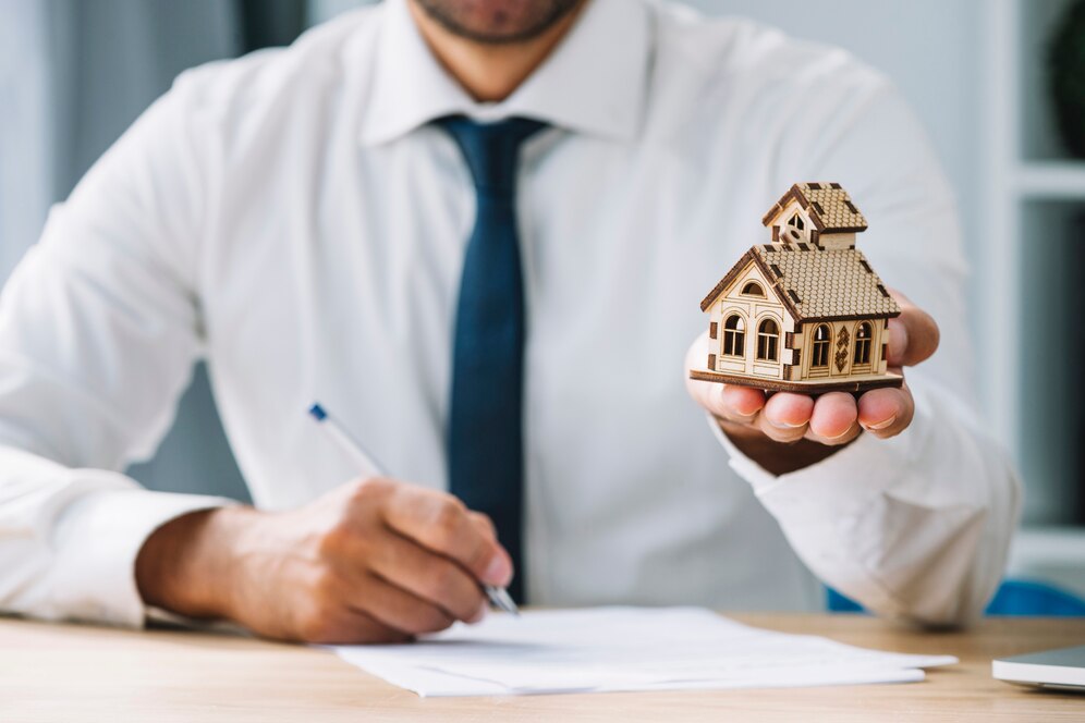 Real estate agent holding a house model while signing documents, symbolizing property transactions with the Best Real Estate Agent in Newport Beach