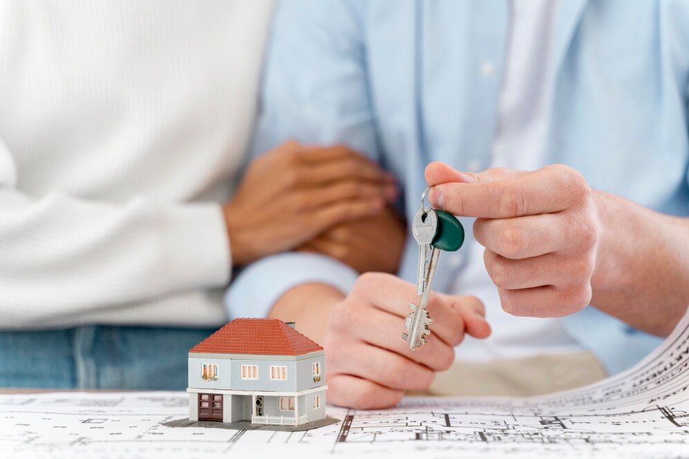 "Top Real Estate Agent in Mission Viejo handing over house keys to a couple with a model house on the table