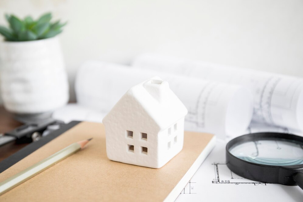 White house model on a notebook with architectural plans in the background, symbolizing property planning with the Best Real Estate Agent in Newport Beach.