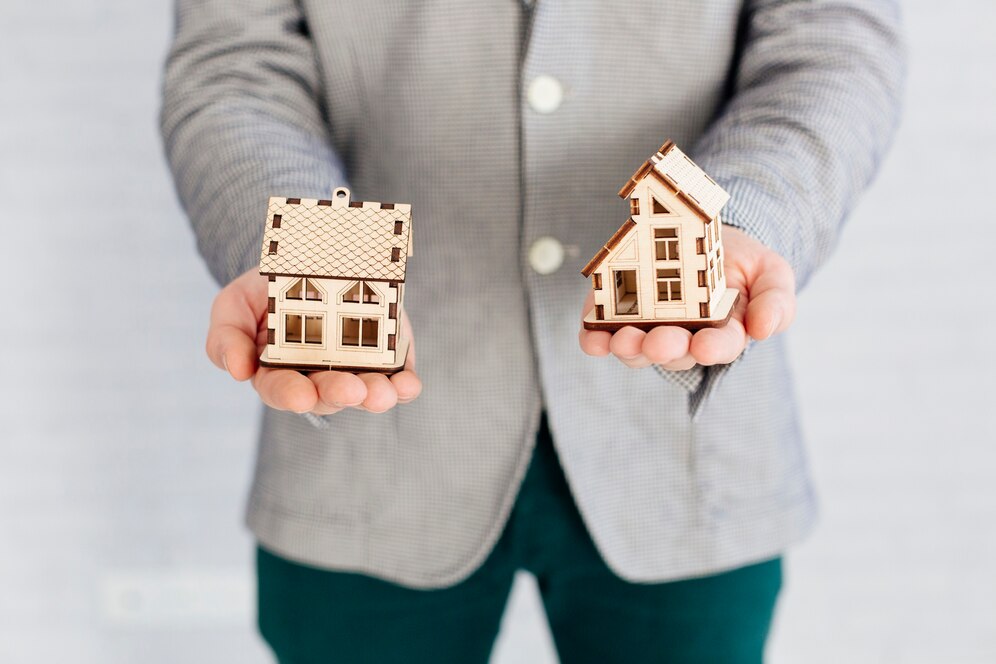 Top real estate agent in Laguna Beach holding two model houses representing property choices.